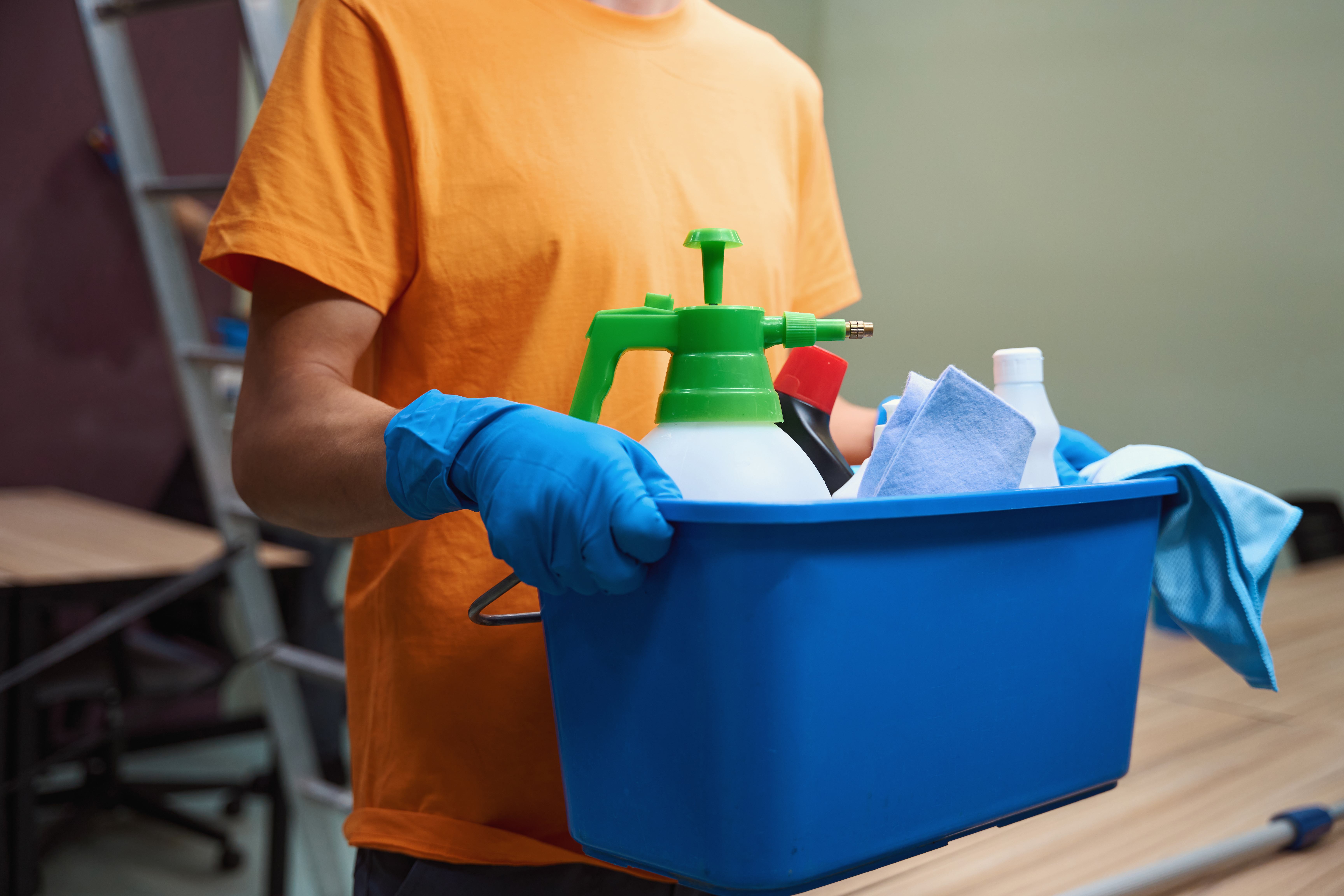 Cropped photo of man in rubber gloves holding a box full of housecleaning equipment